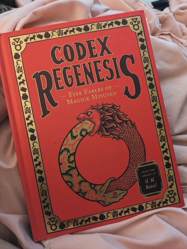 A book called Codex Regenesis. It is a red cloth book with black and gold printed art that depicts two snakes swallowing the other's tail.