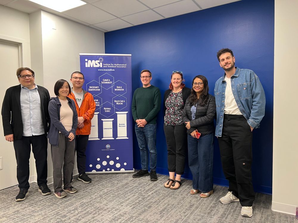 A diverse group of 7 people pose in front of a large banner showing the work of the Institite for Mathematical and Statistical Innovation.