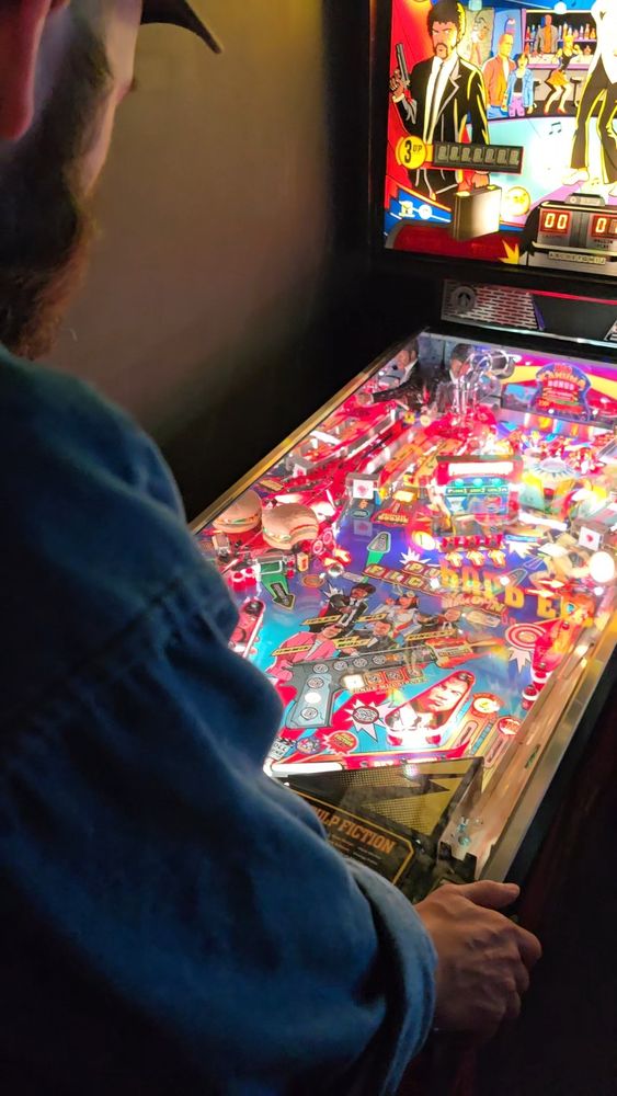 An over the shoulder shot of a bearded man playing Pulp Fiction pinball