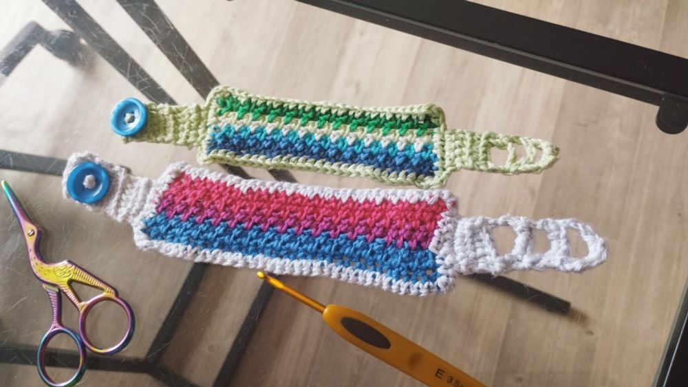 Picture of two bracelets made in crochet. The one above represent the gay male flag, the second the bisexual flag