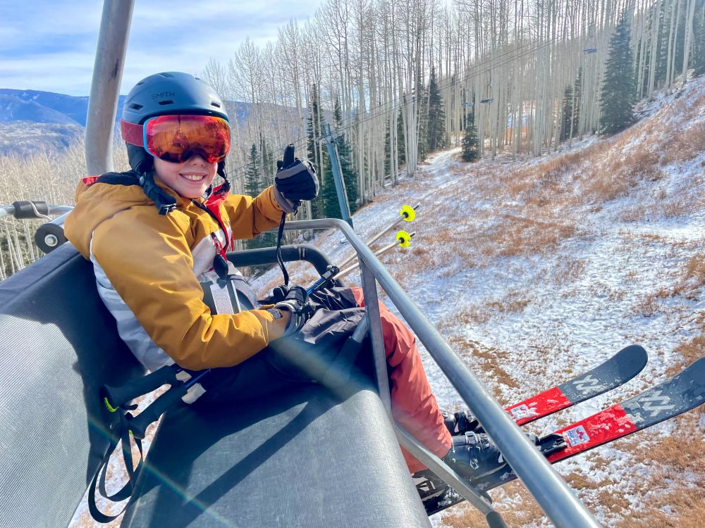 My kid, dressed head-to-toe in ski gear sitting on a chairlift. He's got a huge smile on his face.