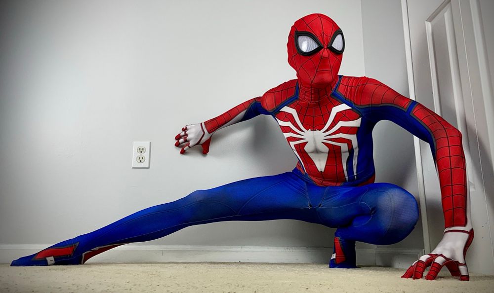 Spidey in his sleek side profile, kneeled and grasping both the floor and wall. His left leg provides support while his right leg stretches out as he diligently eyes his target. The suit is the Advanced Suit made from RPC Studio. It features a deep combination of blue, red, and white accents, including his thick black brimmed lenses that makes hi9s mask pop even more.