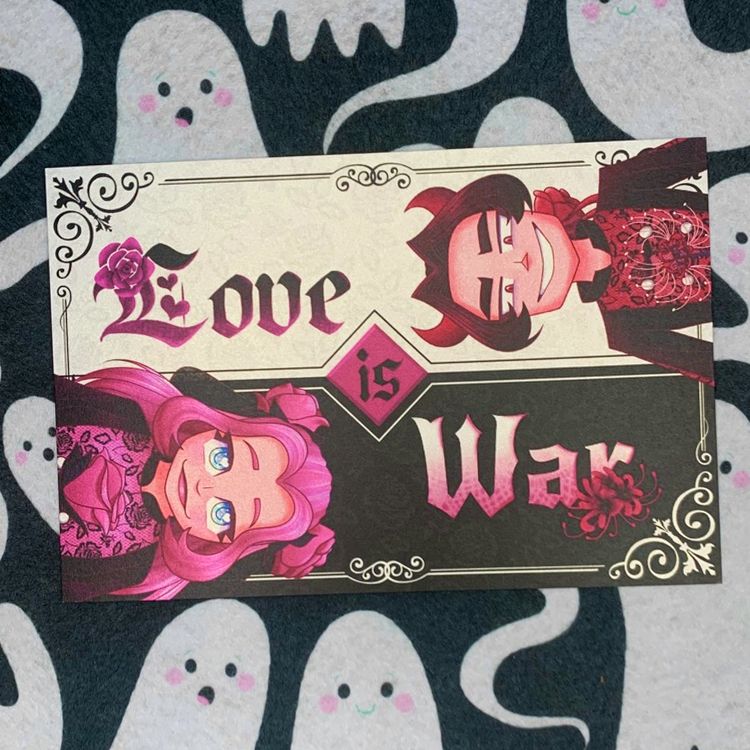 a postcard resting on a black fabric patterned with white ghosts