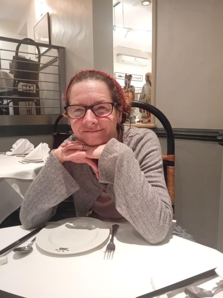 Roz, white lady with red curly hair and glasses, poses in a Chinese restaurant