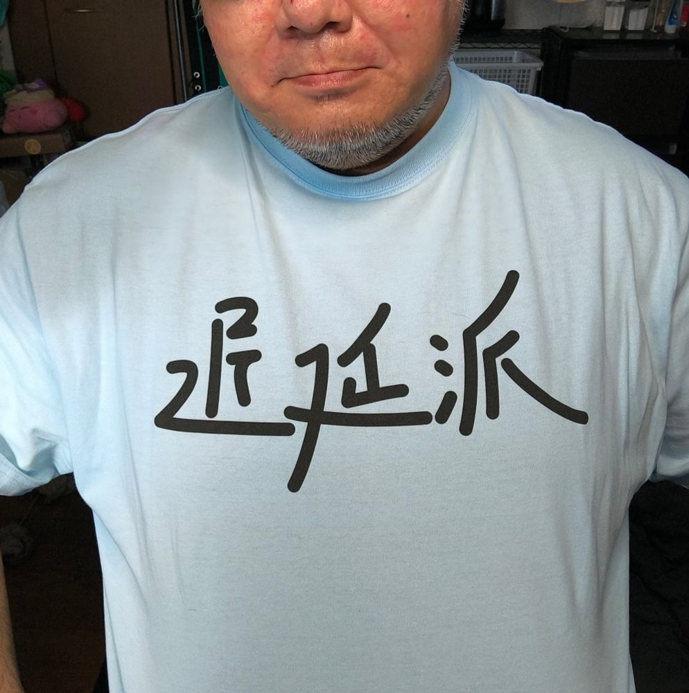 「遅延派通信」のロゴ（手書き風の書体で「遅延派」と書いてある）Tシャツを着た自撮り
