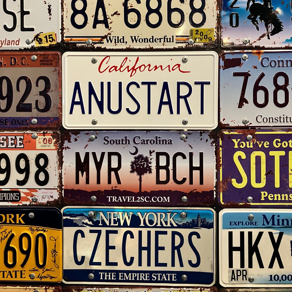 A wall of license plates, including a California plate which reads “ANUSTART”