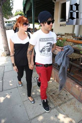 Pete Wentz wearing black beanie, black sunglasses, white tshirt, red skinny jeans, black sneakers holding hands with red haired Ashlee Simpson 