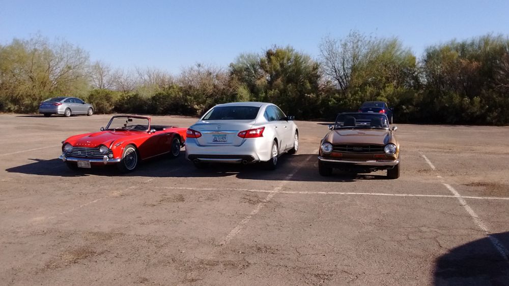 A silver Nissan Altima parked between a red Triumph TR4 and gold Triumph TR6 in a parking lot in Tucson, Arizona