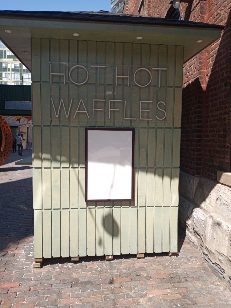 A food hut with an unlit neon sign that says "HOT HOT WAFFLES"