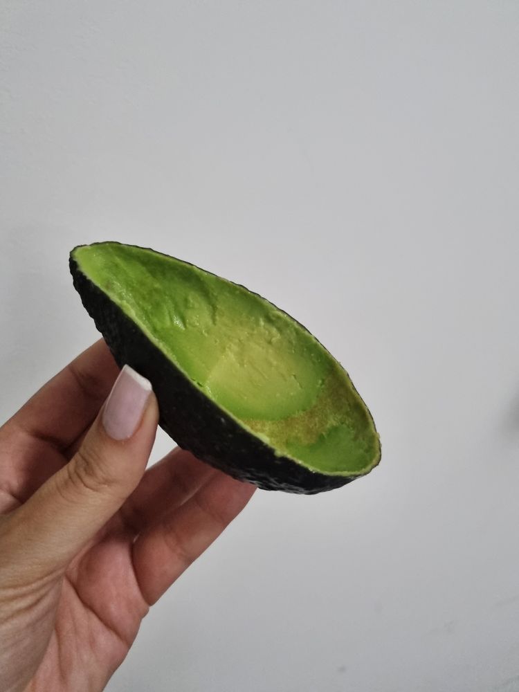 Mão segurando uma casca de avocado sem a polpa, só a casca em formato de cumbuquinha