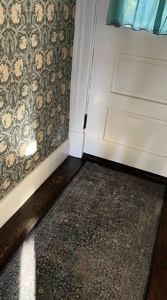 Photograph of the entryway of a home with William Morris wallpaper and a William Morris rug 