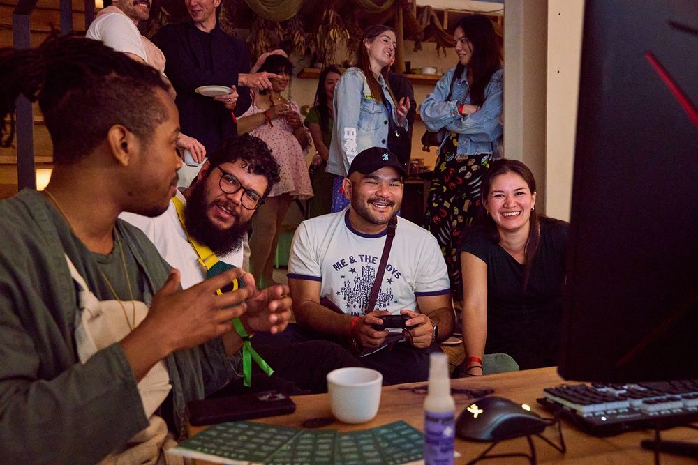 a close-up shot of 4 people seated around a PC demo station. there are people standing and talking in the background next to a tea bar.