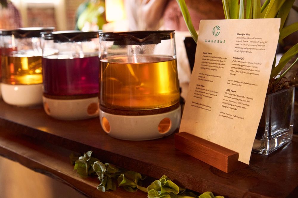 a close-up shot of 3 colorful teas in glass kettles. a Gardens-themed menu details what is in each tea.