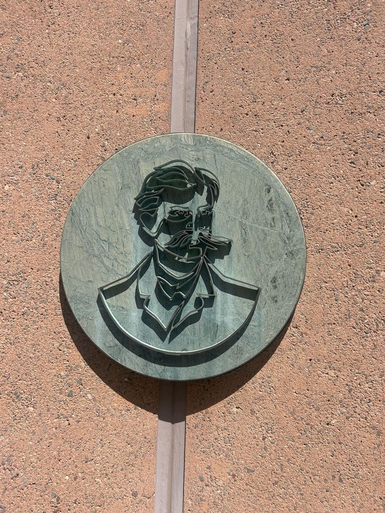 A bronze wire likeness of a rich white man with a rather exaggerated and bushy “English?” or “handlebar?” Mustache depicted