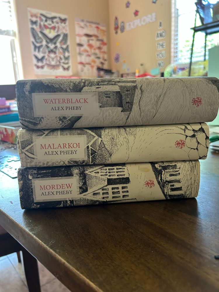 A stack of books showing the so far complete Cities of the Weft series by Alex Pheby: Mordew, Malarkoi, and Waterblack 