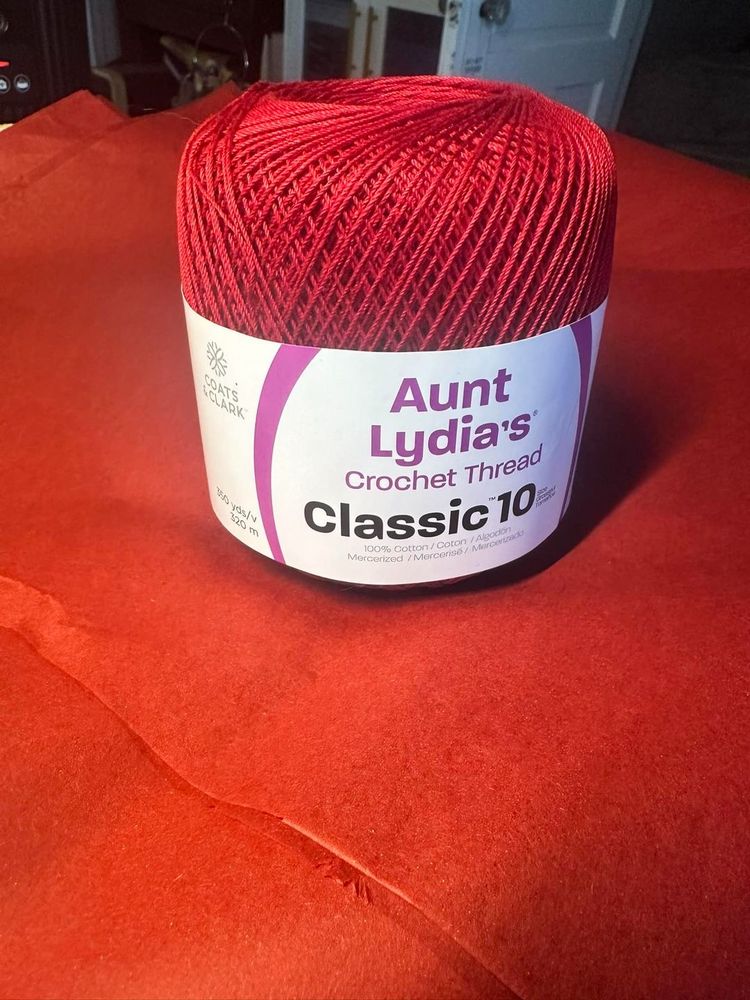 A spool of bright red crochet thread still in the wrapper, which is branded "Aunt Lydia's."