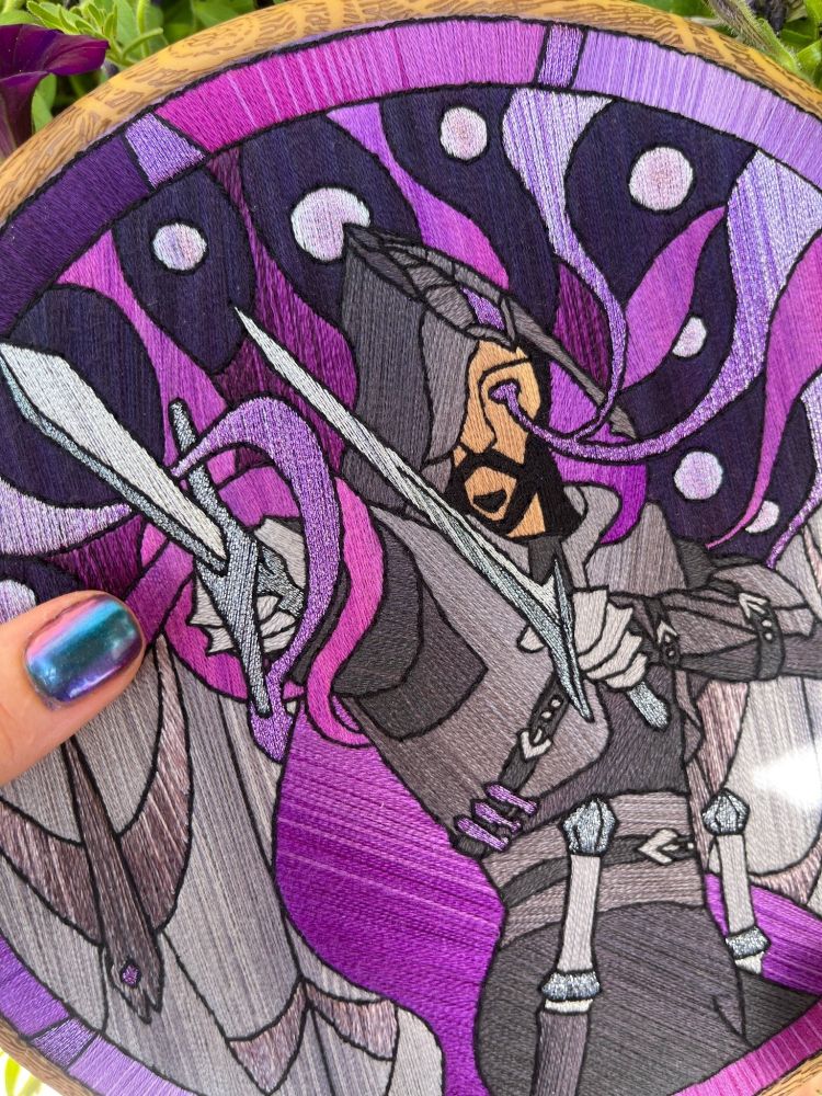 A close up a hand holding the Lucanis embroidery, showing the stitching details closer