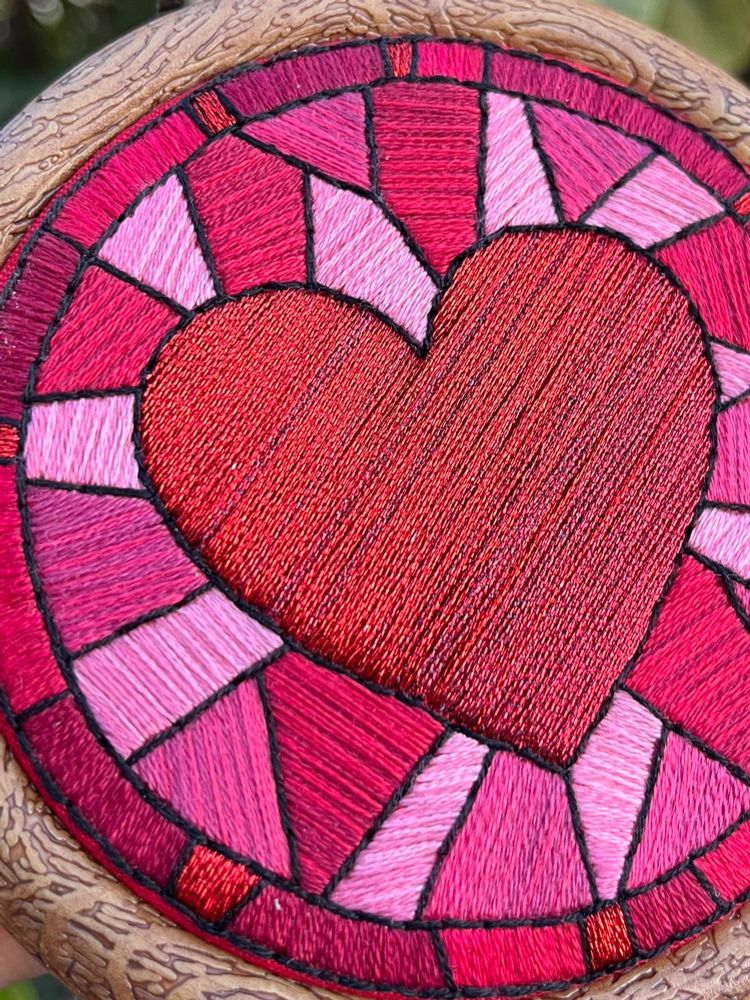 A close up photo of the embroidery showing details in the stitching, and the metallic thread used to make the read heart in the center stand out more from the surrounding cotton threads