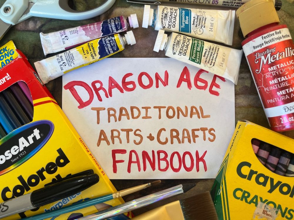 A piece of paper with the words "Dragon Age Tradition Arts & Crafts Fanbook" painted on it in red and copper acrylic paint. Surrounding it are art supplies like paint tubes, paintbrushes, sharpies, scissors, and boxes of colored pencils and crayons. 