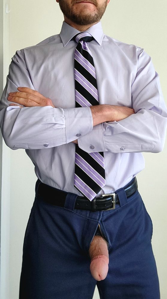 Myself in a lavender dress shirt tucked into dark blue pants and a black belt. My arms are crossed. Wearing a purple/black striped tie tied in a windsor knot. My semi hard cock is out of my fly. 
