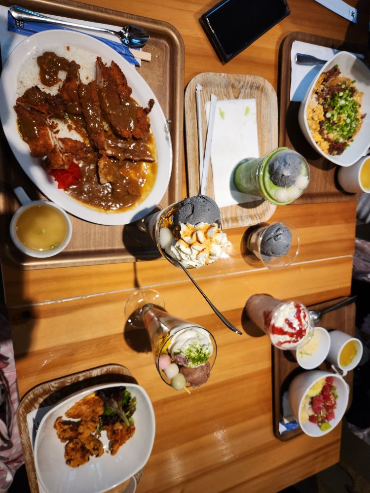 Chicken katsu curry, karaage, katsudon, and salmon dish, with various sweets and drinks, on a wooden table 