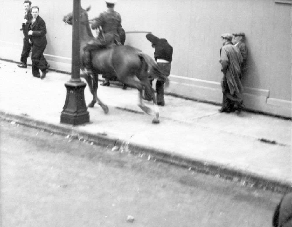 Policeman on horseback strikes man on sidewalk.