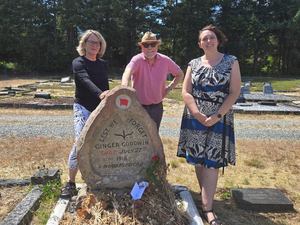 Three people stand by Ginger Goodwin's headstone. Lest We Forget. Ginger Goodwin Shot July 27th 1918. A Workers Friend.