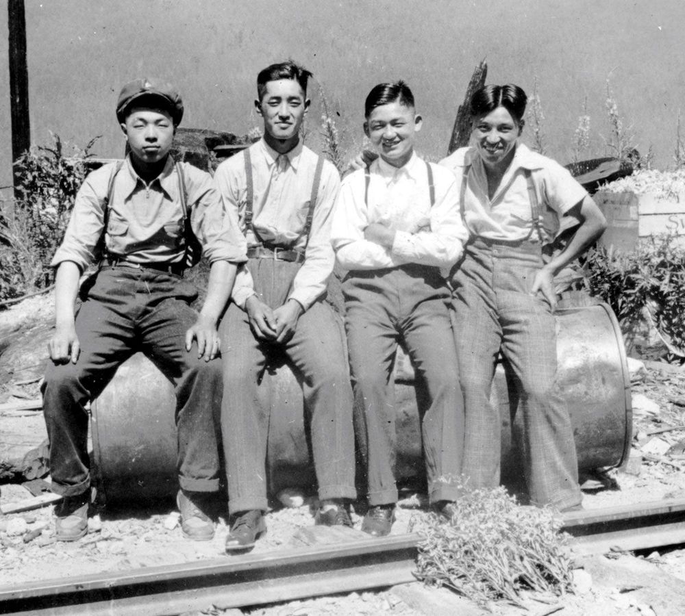 Four Japanese men sitting beside railway track.