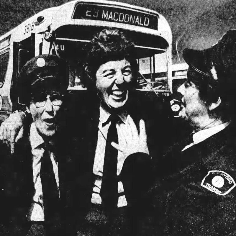 Three women in transit uniforms pose in front of number 23 Macdonald bus.