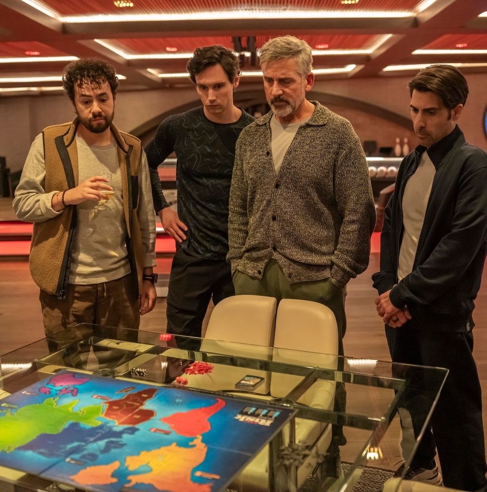 Ramy Youssef, Cory Michael Smith, Steve Carell, and Jason Schwartzman in Mountainhead. They are standing in a group looking down at a Risk board on a table.