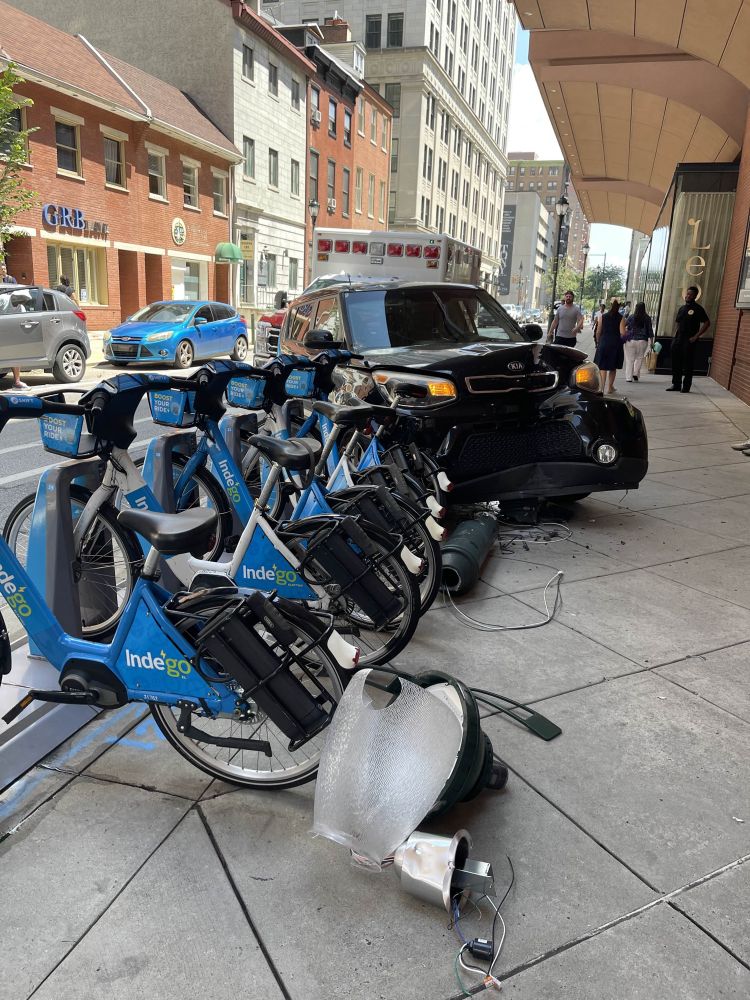 Image of black Kia crashed onto sidewalk with lamp post and bike share rack hit