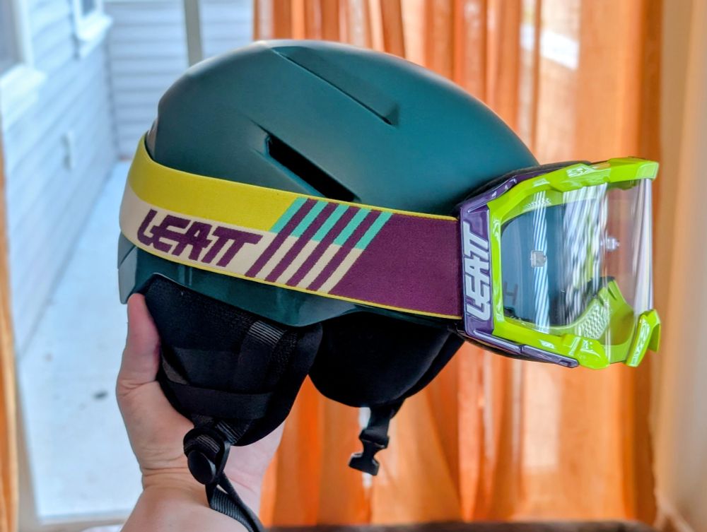 A teal green helmet with yellow and purple goggles