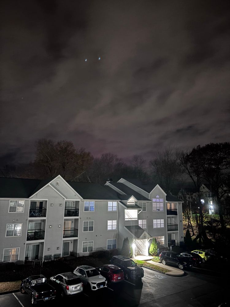 apartment building with a mostly gray cloudy sky with a tiiiiny bit of pink aurora visible at the very edge of the treeline 