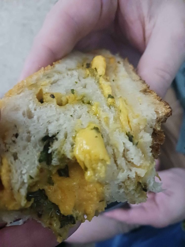 Hands holding a slice of yeast bread with ribbons of melted colby and herbs baked inside