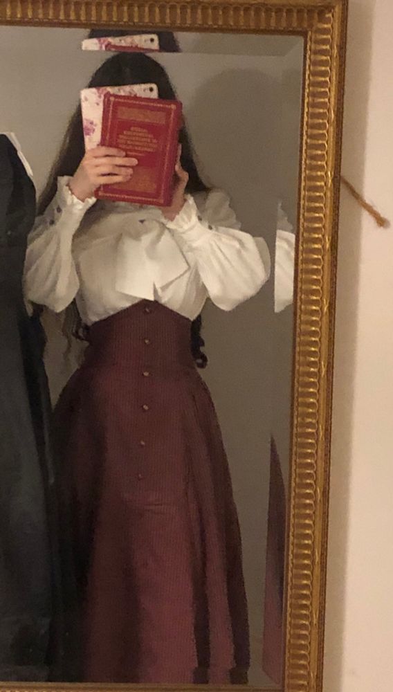 An outfit picture taken through a large mirror. I’m wearing a long dark red high waisted skirt with boning around the waist to keep the fabric up (with pockets!) and long sleeved blouse, both from Forest Wardrobe, with my hair down . I am holding my Mother’s copy of Alice’s Adventures in Wonderland from when she was a child to cover my face as the cover is a beautiful red.