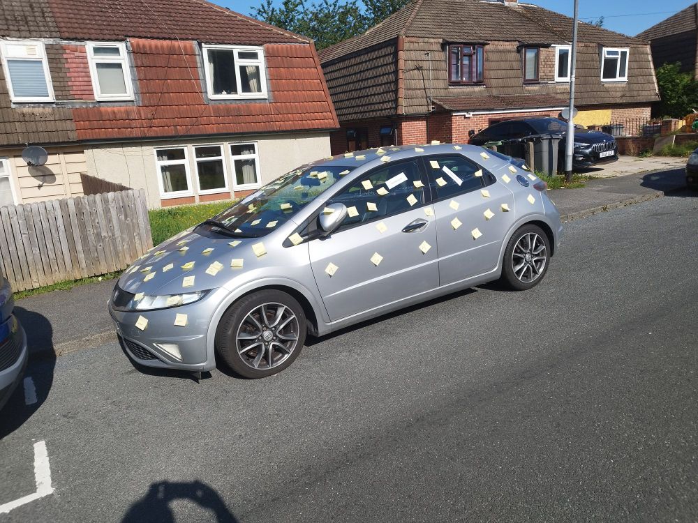 A wide shot of the car from the previous image. The post-its are not readable from this distance, but it is clear they are all over the car
