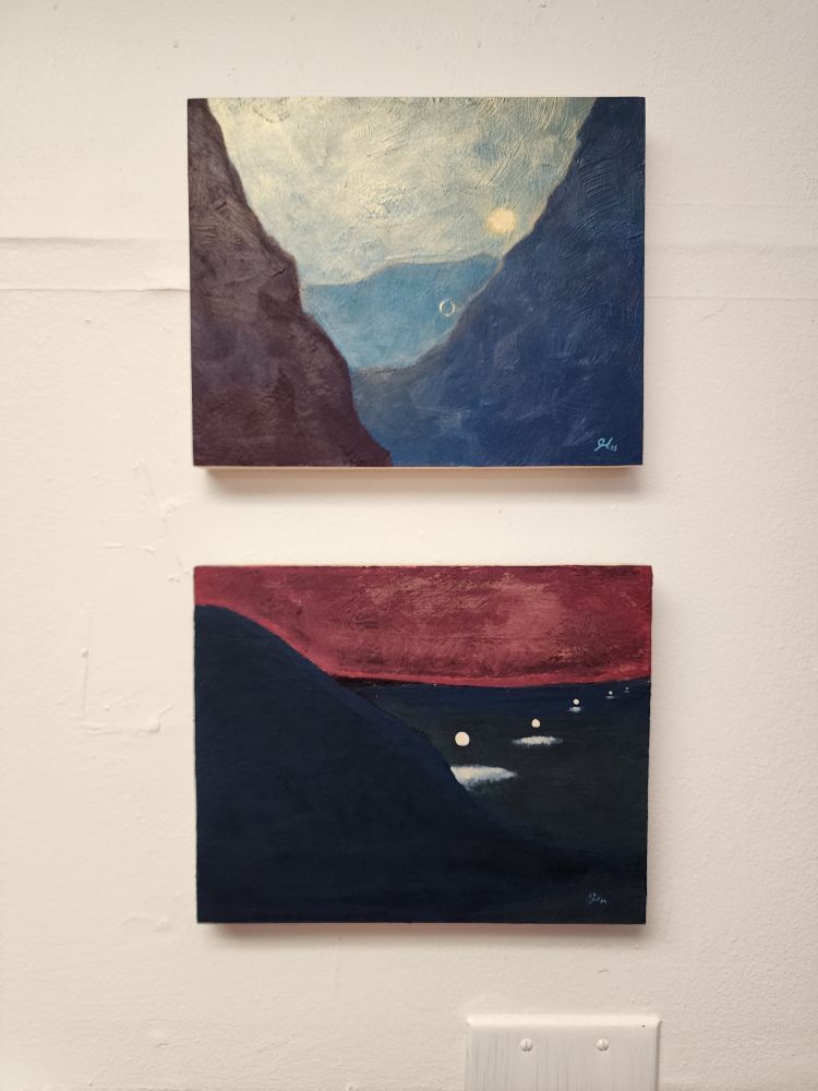 Two rectangular paintings. The top is mostly different shades of blue with mountain type shapes creating a canyon with a golden sun. The lower is red and black sowing an open desert with a series in 5 mysterious light globes. 
