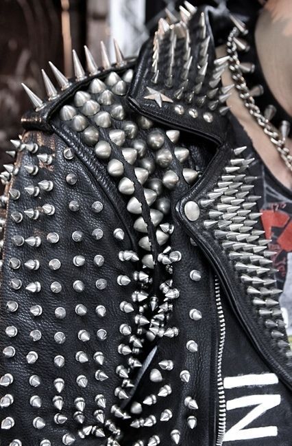 A close-up photo of a punk rock style leather jacket liberally studded with sharp spikes of various kinds and lengths, as well as a spiked leather choker around the neck.