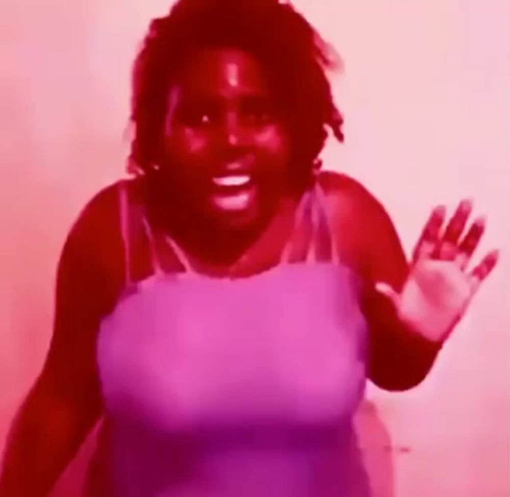 a woman in a purple tank top is waving her hand in a red light .