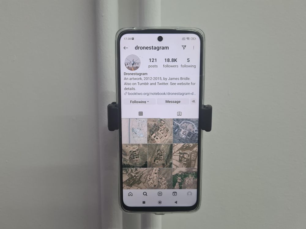 James Bridle's work Dronestagram on display on a mobile phone pinned to the wall in an exhibition.