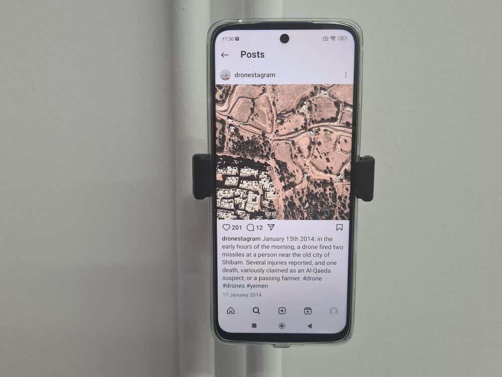 James Bridle's work Dronestagram on display on a mobile phone pinned to the wall in an exhibition.