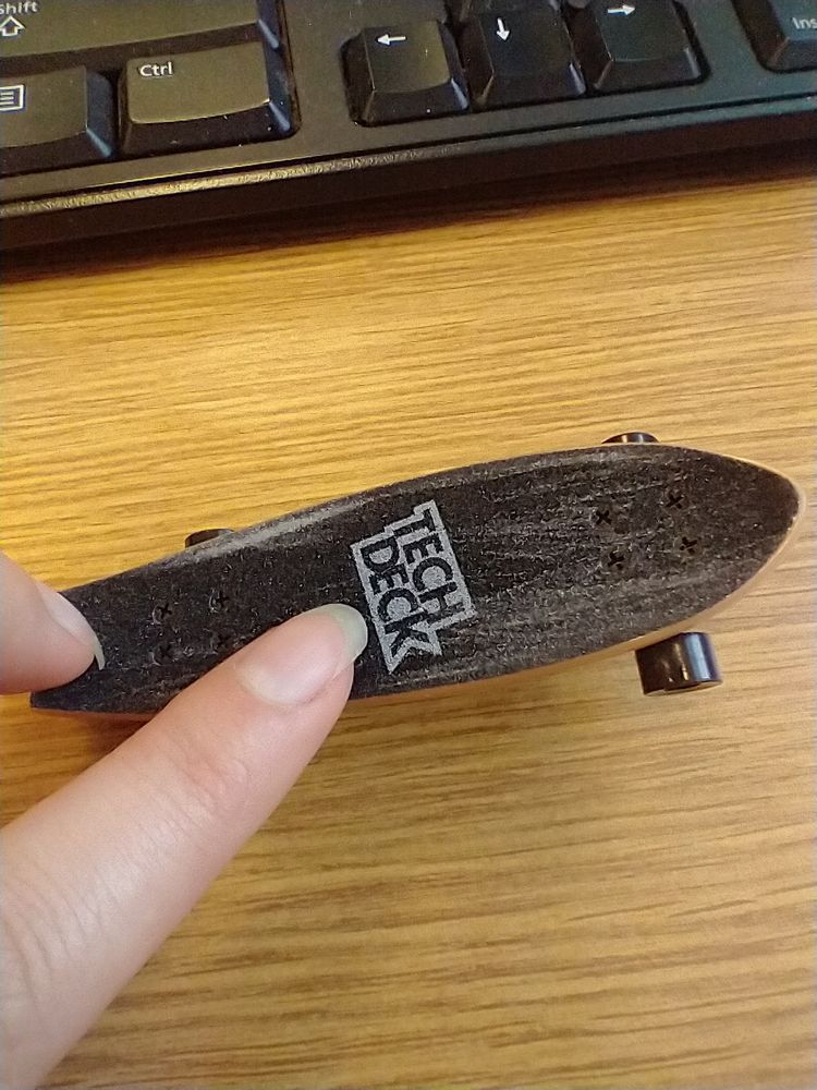 A finger on a tech deck that has obviously been used as a nail file.