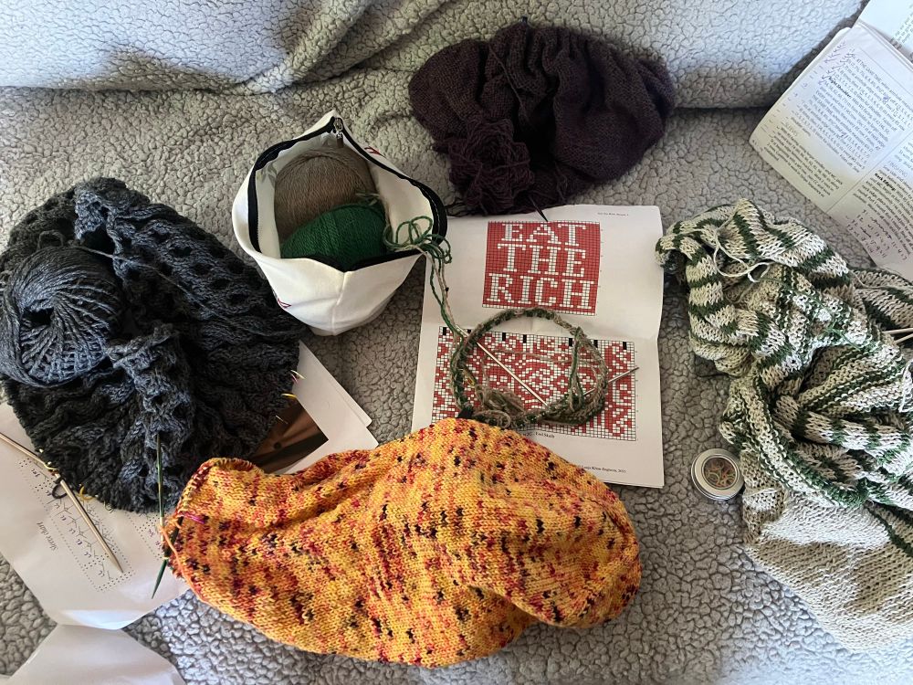 A pile of knitting projects in various states of progress lay on a couch. 

Clockwise from top:
The Lenore cardigan by Audrey Borrego is in the beginning stages, abandoned since June due to the tedium of flat worked fingering weight stockinette. The deep heathered purple Palette yarn beckons as the weather changes. 

The moss green and oatish cream striped Parnell pullover remains languishing on needles, despite the recent progress of seaming the shoulders and picking up and knitting half a sleeve. 

The Musselburgh hat is growing steadily thanks to regular meetings that could have been emails and webinars that could have been asynchronous. A handy project for all occasions that accompanies me everywhere. 

The Billie pullover by Sari Nordlund in thunder cloud gray worsted merino from Knitting for Olive is coming along… and I’m afraid that my cable honeymoon is nearing an end! What began as a fascinating journey of twists and turns is beginning to feel like a slog… but ski season is approaching, and the knitting group is planning to wear out Billies for opening weekend :)

In the center the beginning of a hat that deserves more attention, but has been cast aside multiple times in the name of sweaters. Maybe if it’s the only project the knitter has on a plane it will finally get the focus it deserves. 