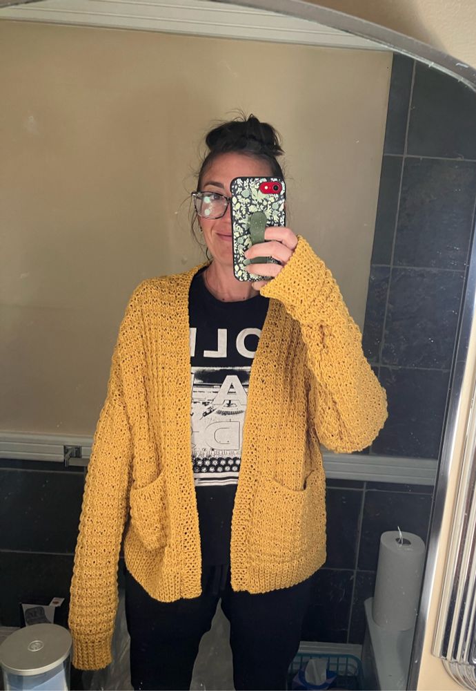 A woman models her newly completed yellow cardigan, complete with pockets and sleeves that are far too long but make for an extra cozy fit. 