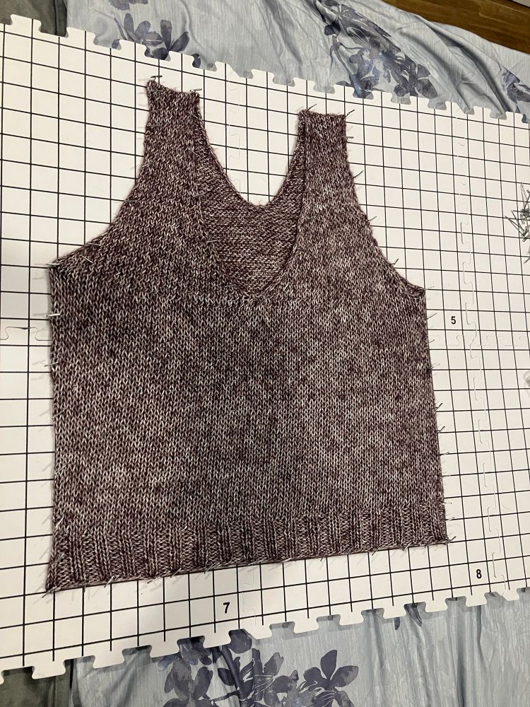A hand knit purple tank top pinned and blocked on a grid, almost ready to wear. 