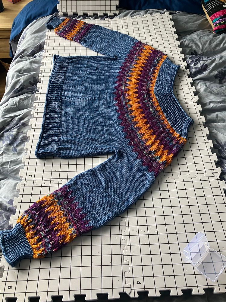 The Easy V sweater on some blocking mats- this yarn (malabrigo rios) bloomed so much in the wash I thought I had ruined the sweater! No pinning necessary- thankfully it shrunk back to the intended size and stitches became soft and smooth as it dried. 

The sweater is a denim blue with zigzagging stripes of golden yellow, tonal purple/teal/pink, and rich plum on the yoke and cuffs. The hems of the sweater feature a roll past the ribbing giving the sweater a relaxed and flowing fit.
