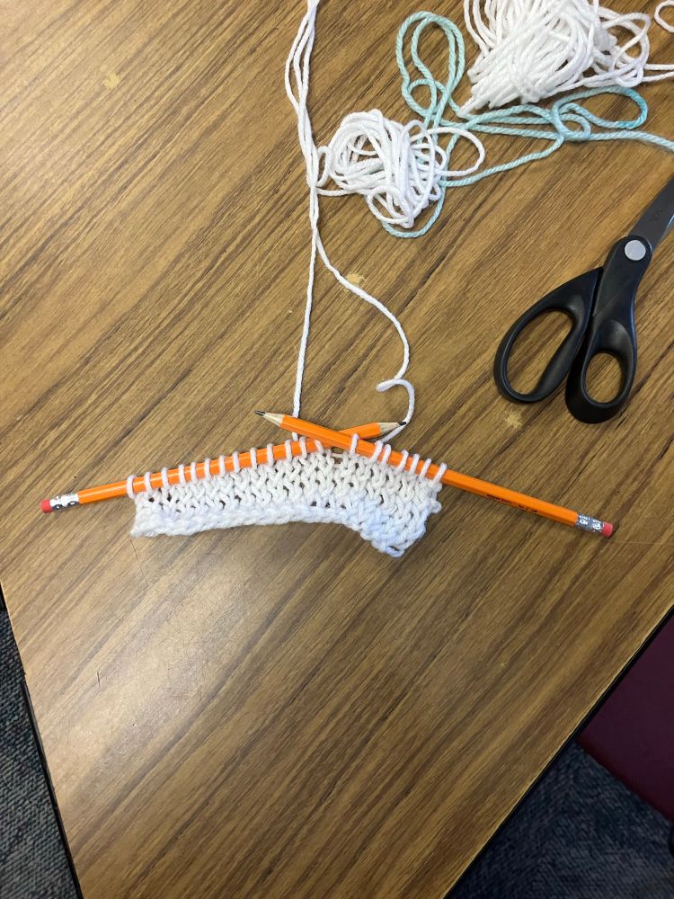 The beginning of a knit project in white yarn cast on and worked with #2 pencils 