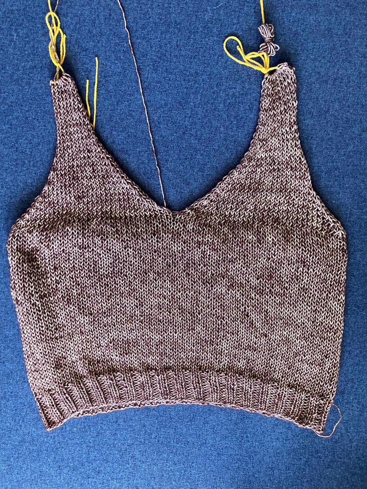 A light purple hand knit tank top against a blue background. Strings of yarn poke out, waiting to be finished and woven in. 