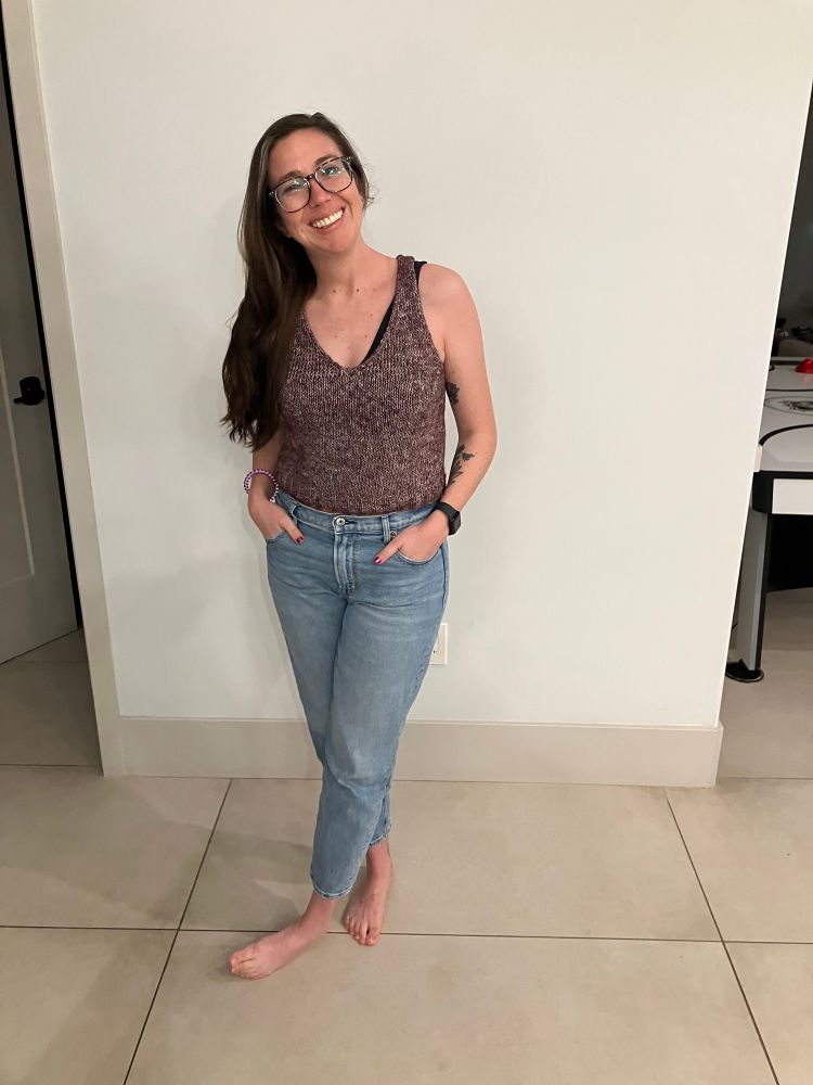 A woman poses in a hand knit purple tank top and jeans
