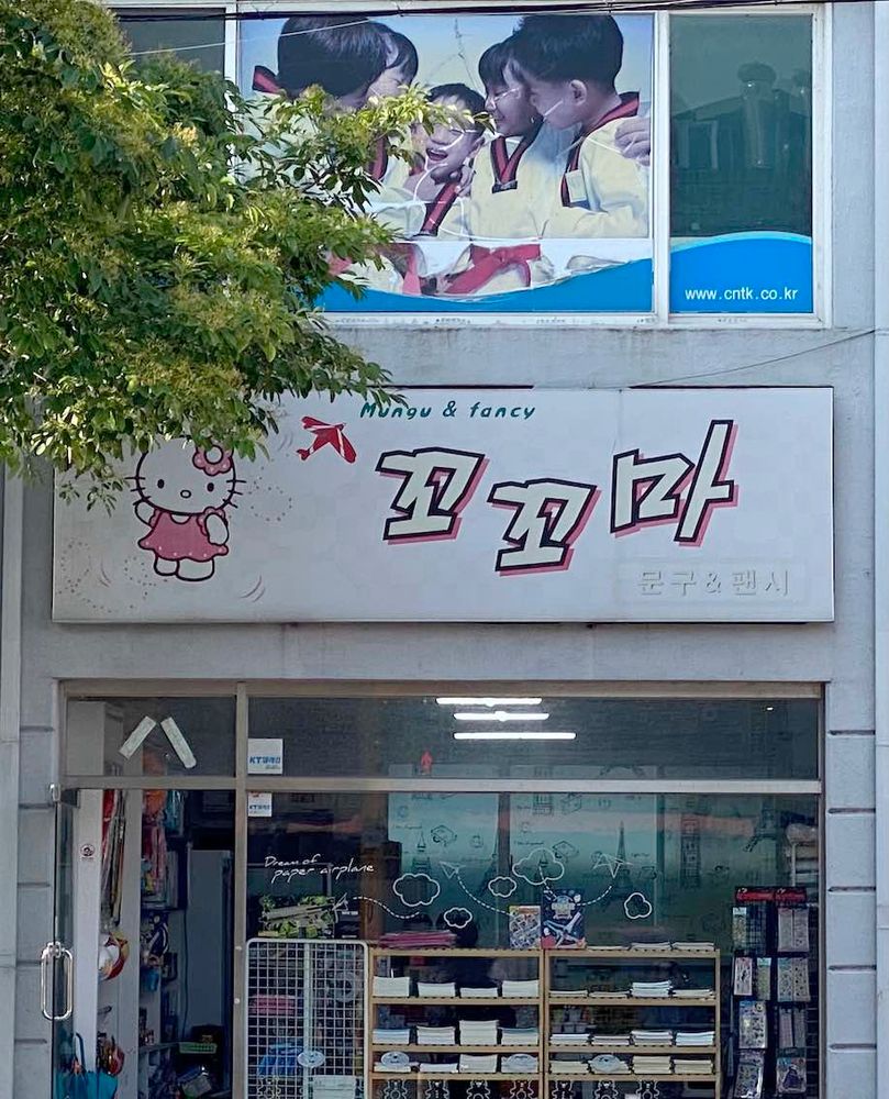 Photo of a storefront in Korea. The sign has an image of Hello Kitty on it and says: 꼬꼬마 Mungu & fancy 문구 & 팬시.
The shop is near an elementary school, it sells stationery and snacks to a clientele of small children. The name is based on 꼬마 'kid'.